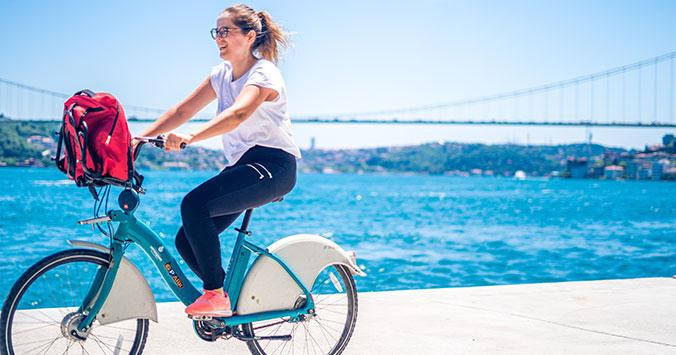 Chica haciendo la acción de pedalear en una bicicleta frente al mar / UNSPLASH