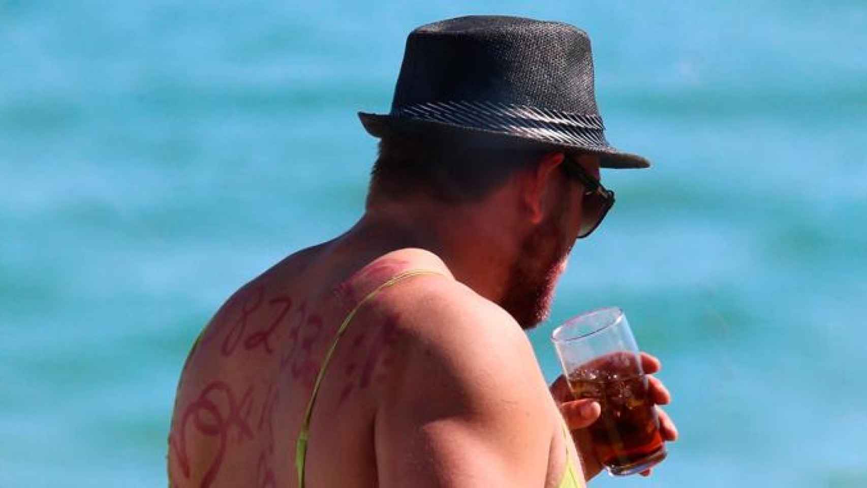 Un hombre disfrazado bebe alcohol en una playa