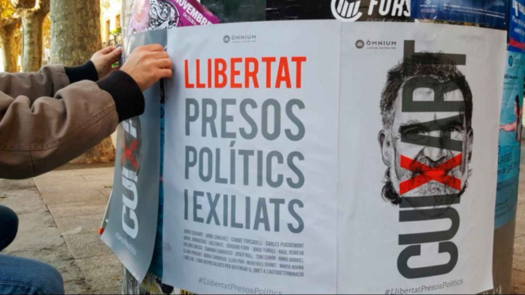 Un voluntario pega los carteles de Òmnium para pedir la libertad de los líderes independentistas / TWITTER