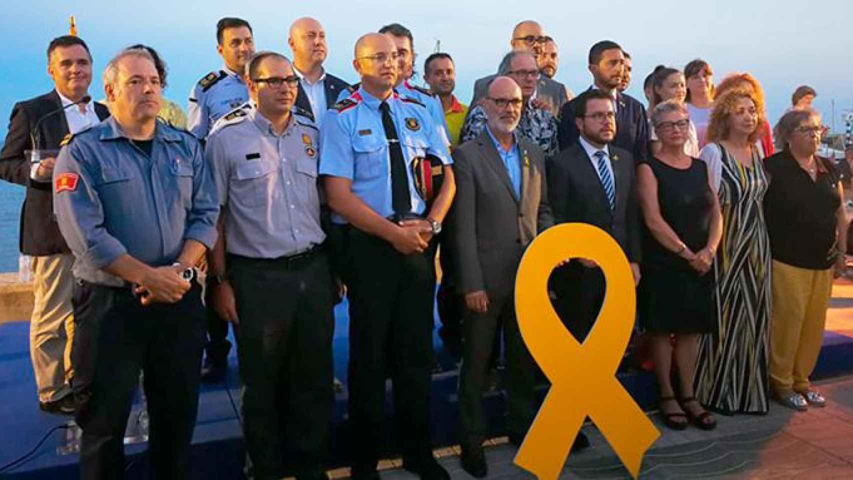 Varios miembros del Govern y de los Mossos celebran el primer aniversario de los atentados del 17A en Alcanar (Tarragona) con un gran lazo amarillo / CG