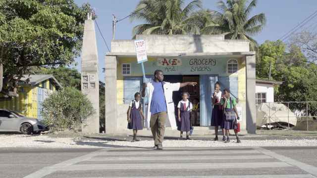 Un adulto ayuda a cruzar por un paso de peatones a unos niños que salen de la escuela / ABERTIS