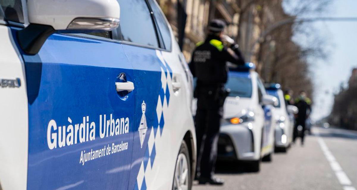 Un agente de la Guardia Urbana de Barcelona junto a un coche patrulla / GUARDIA URBANA