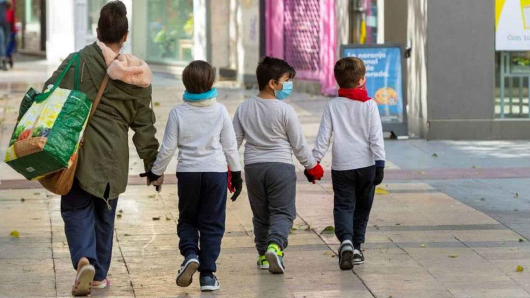 Una mujer pasea con tres niños con mascarillas / EFE