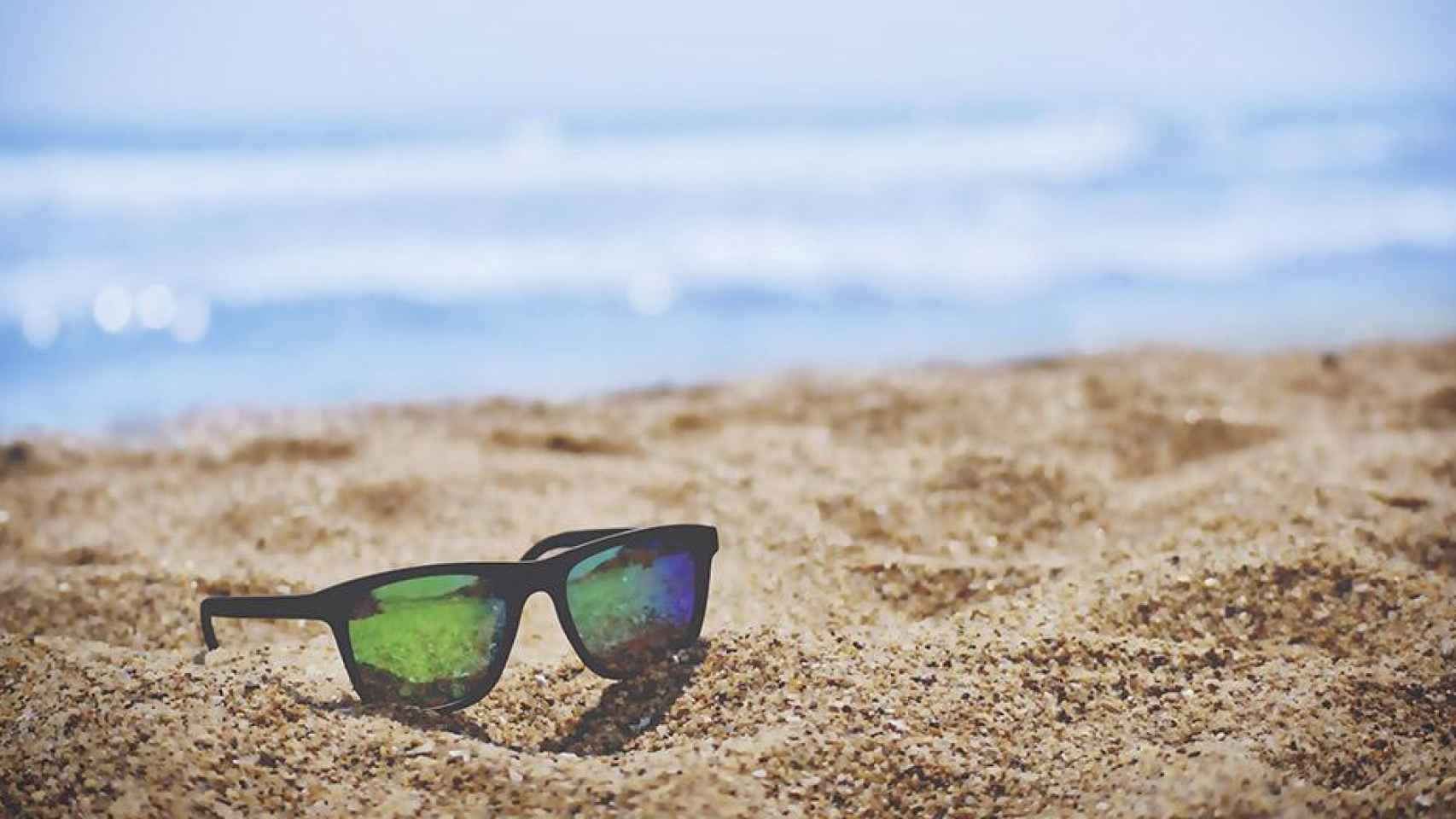 Gafas de sol en la arena de una playa / UNSPLASH
