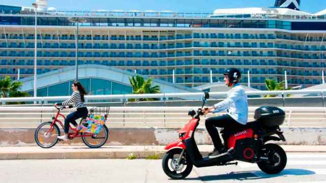 Imagen de una moto eléctrica y una bicicleta Scoot frente a un crucero en Barcelona / CG