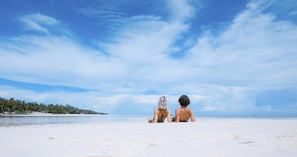 Una pareja toma bronceado en la playa / UNSPLASH