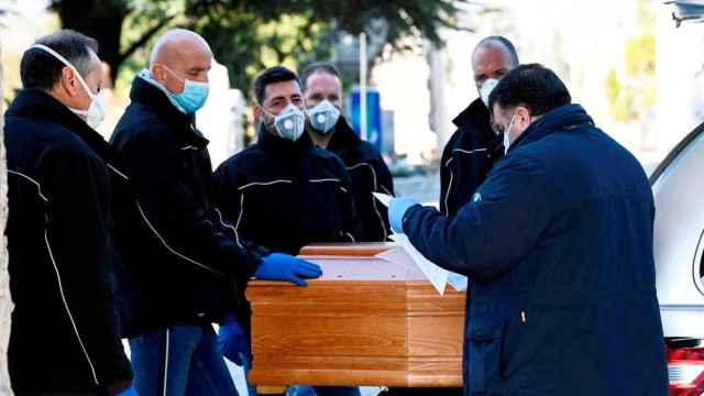 Imagen de operarios con mascarilla de una funeraria de Madrid trasladando un féretro / EFE