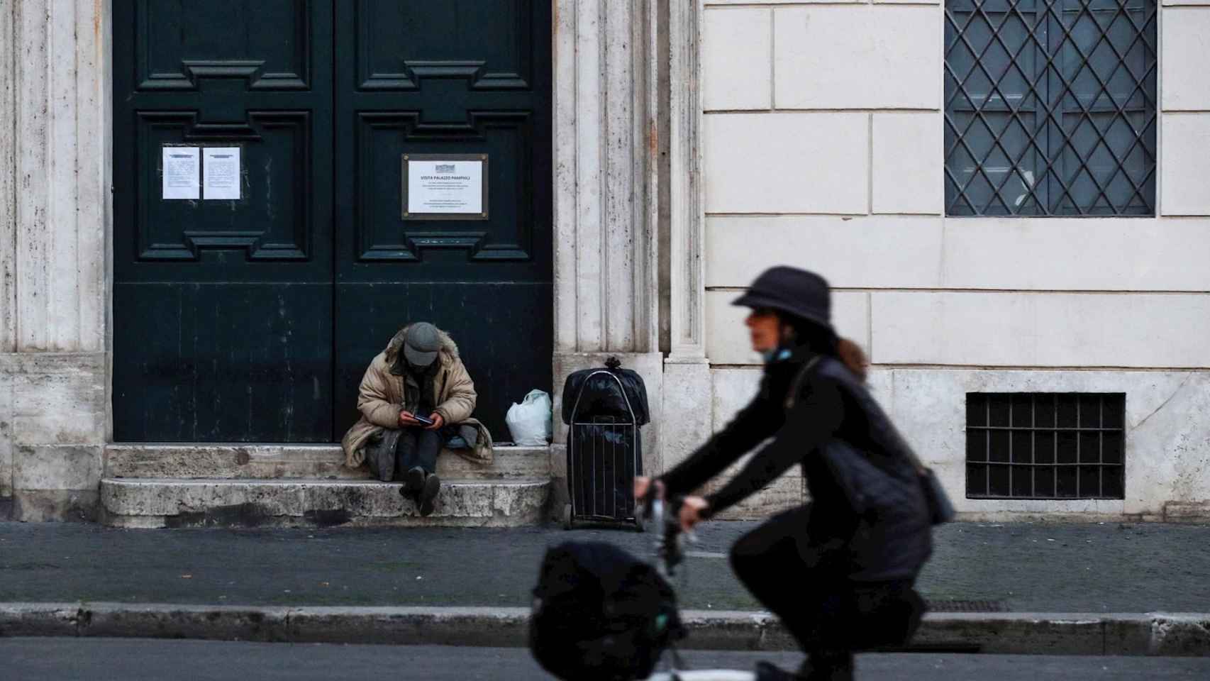 Persona sin hogar y mujer en bicicleta en las calles de Roma, Italia, en plena pandemia del coronavirus / EFE