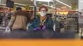 Una mujer mayor con mascarilla y guantes compra en un comercio de alimentación de Barcelona durante el estado de alarma por coronavirus / EP