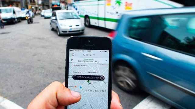 Imagen de la aplicación de servicios VTC Uber con tráfico en una calle de Barcelona de fondo / CG