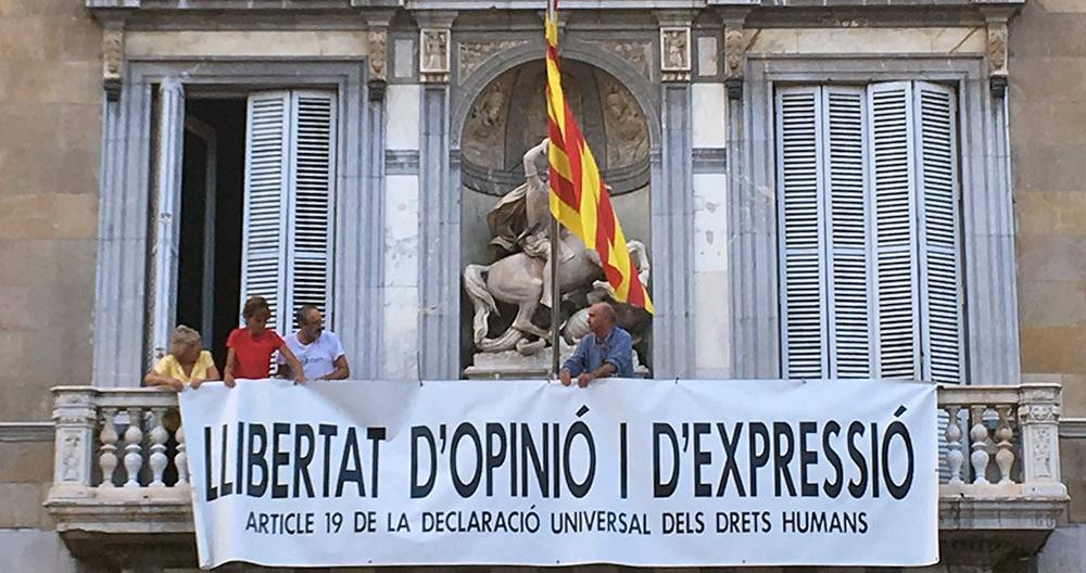 Lluís Llach (d), Antoni Baños (2 d) y Sílvia Bel (2 i) cuelgan una pancarta a favor de la libertad de opinión y expresión en el Palau de la Generalitat