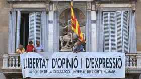 Lluís Llach (d), Antoni Baños (2 d) y Sílvia Bel (2 i) cuelgan una pancarta a favor de la libertad de opinión y expresión en el Palau de la Generalitat