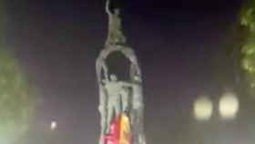 Un joven trepa el monumento a los Castellers para colocar una bandera de España