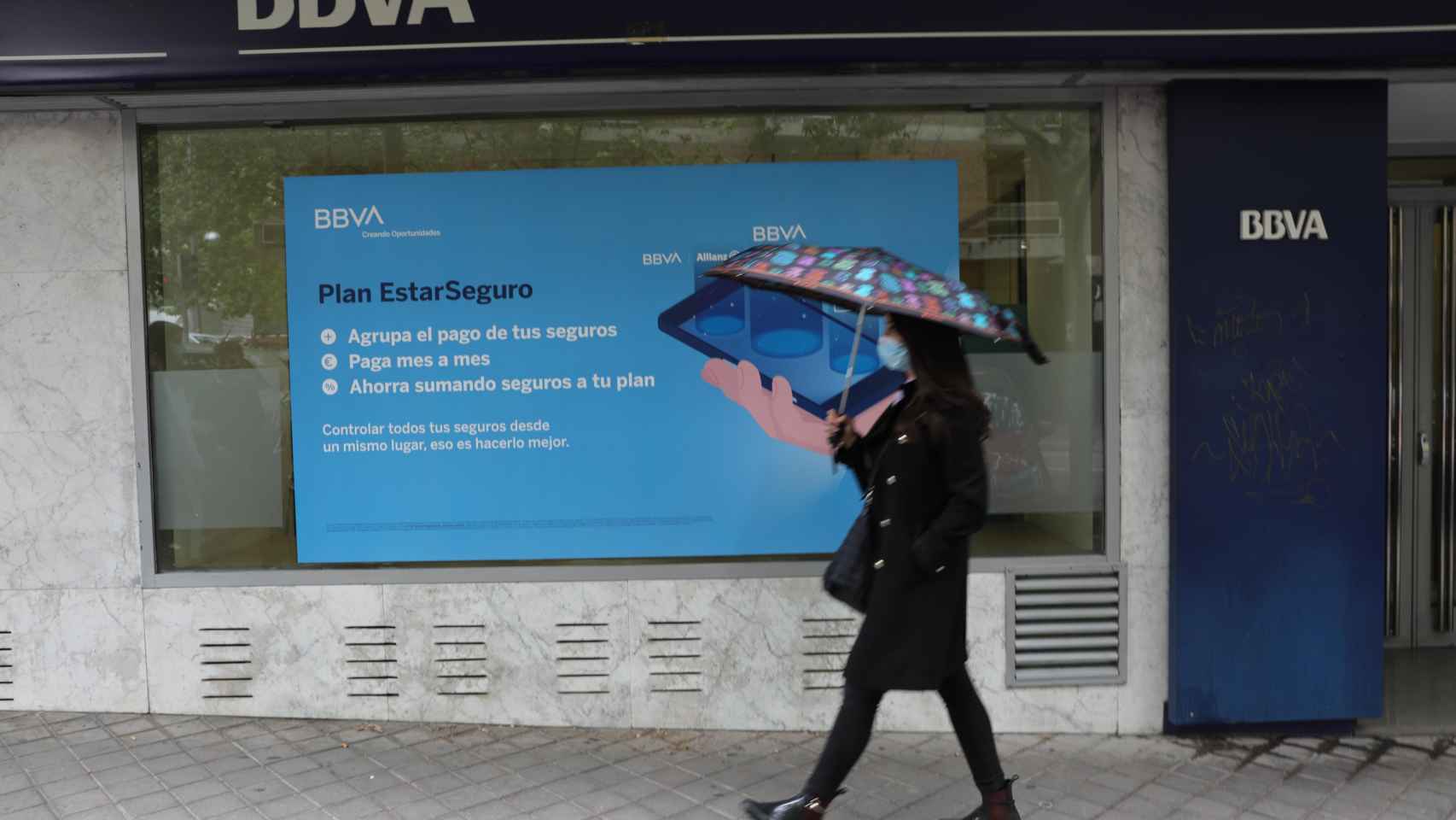 Una persona pasa por delante de la puerta de una oficina del BBVA en Madrid, en una imagen de archivo / EUROPA PRESS
