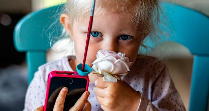 Una niña sujeta un móvil mientras huele una rosa / PIXABAY