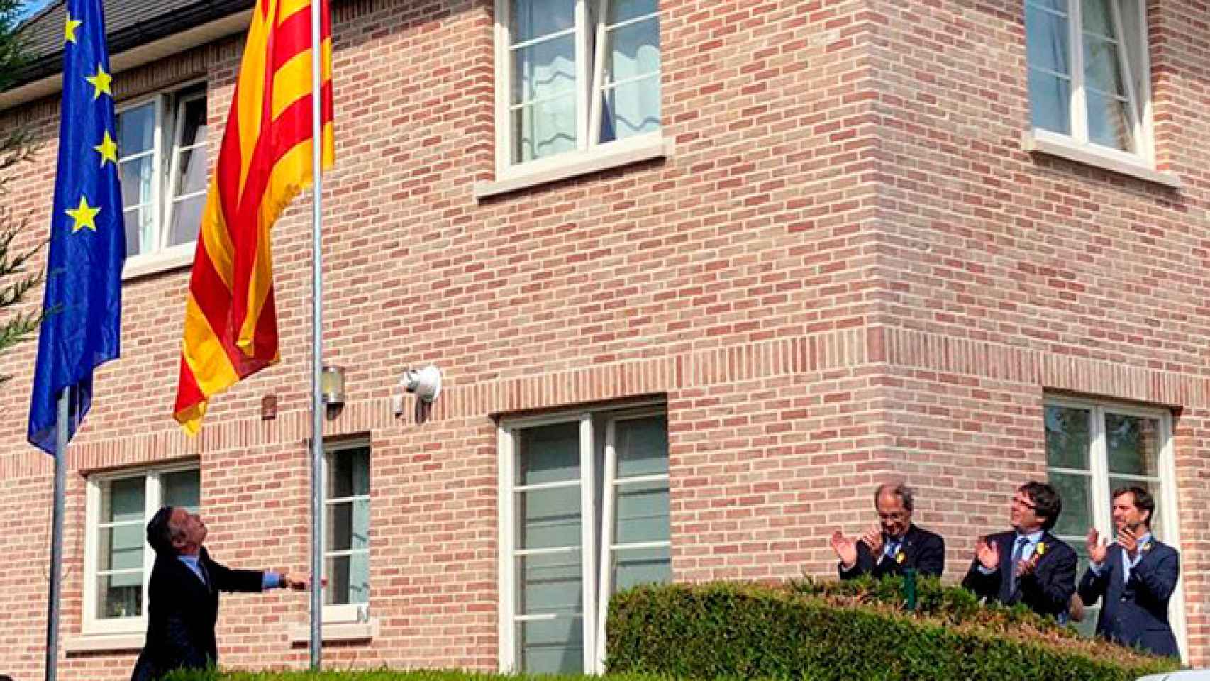 El expresidente de la Generalitat Carles Puigdemont (c), el presidente Quim Torras (i) y el exconsejero Toni Comín (d) aplauden el izado de la bandera catalana en los jardines de la llamada Casa de la República / EFE