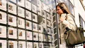 Una foto de archivo de una mujer mirando pisos anunciados en una agencia inmobiliaria tradicional startups