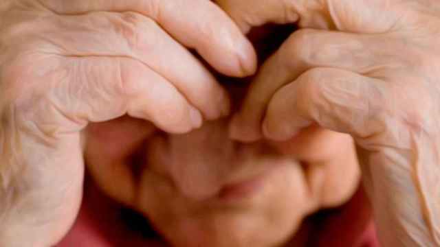 Una mujer anciana cubriéndose la cara con sus manos