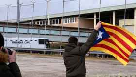 El autobús que traslada a los independentistas presos, al fondo, ante una persona con la bandera secesionista catalana / EP