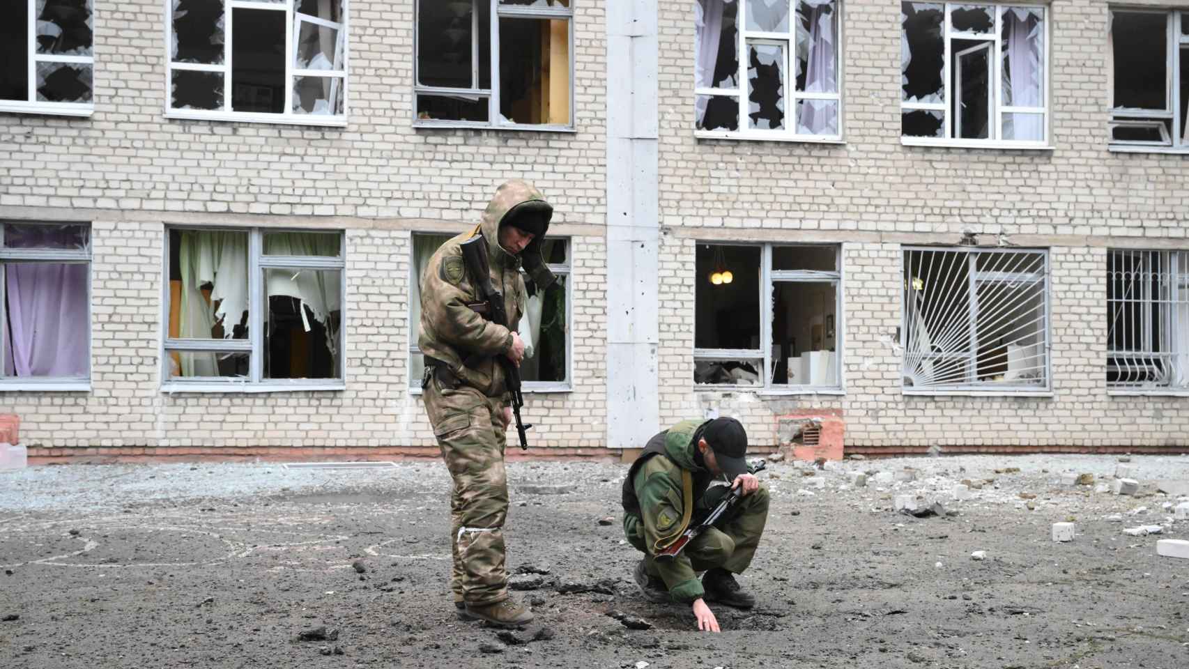 Militares rusos inspeccionan el pavimento de hormigón dañado frente a la escuela, que también sufrió daños como consecuencia de los bombardeos / EP