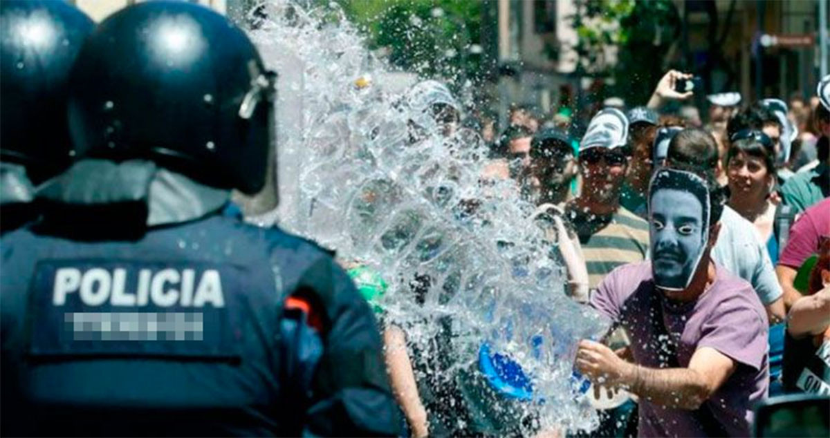 Uno de los okupas del Banc Expropiat de Gràcia lanza un cubo de agua a una de sus víctimas, un agente de los Mossos. La asociación de víctimas de okupas llega a Cataluña / EFE