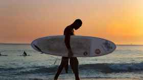 Un surfista abandona una playa al atardecer / CG