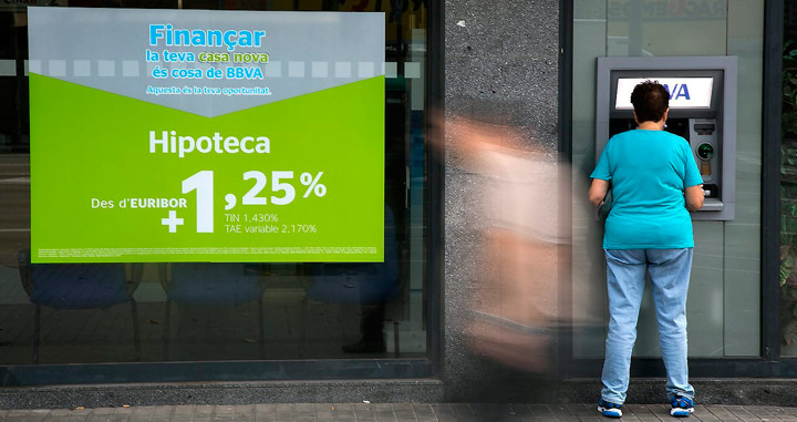 Imagen de una consumidora retirando efectivo de una entidad bancaria junto a publicidad de hipotecas / EFE