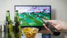 Dos personas toman el aperitivo mientras ven el fútbol en su televisor / PEXELS