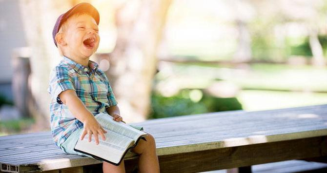 Niño riendo con un libro abierto / UNSPLASH