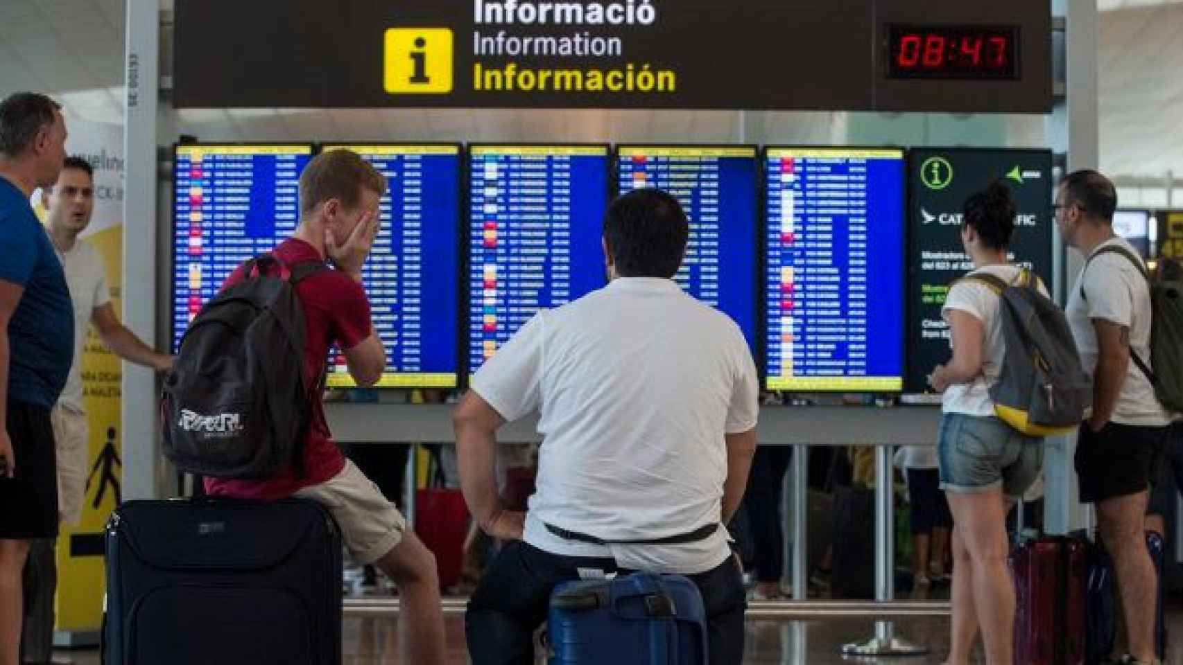 Imagen de dos pasajeros que observan la pantalla de horarios de los vuelos en el Aeropuerto de Barcelona-El Prat / EFE