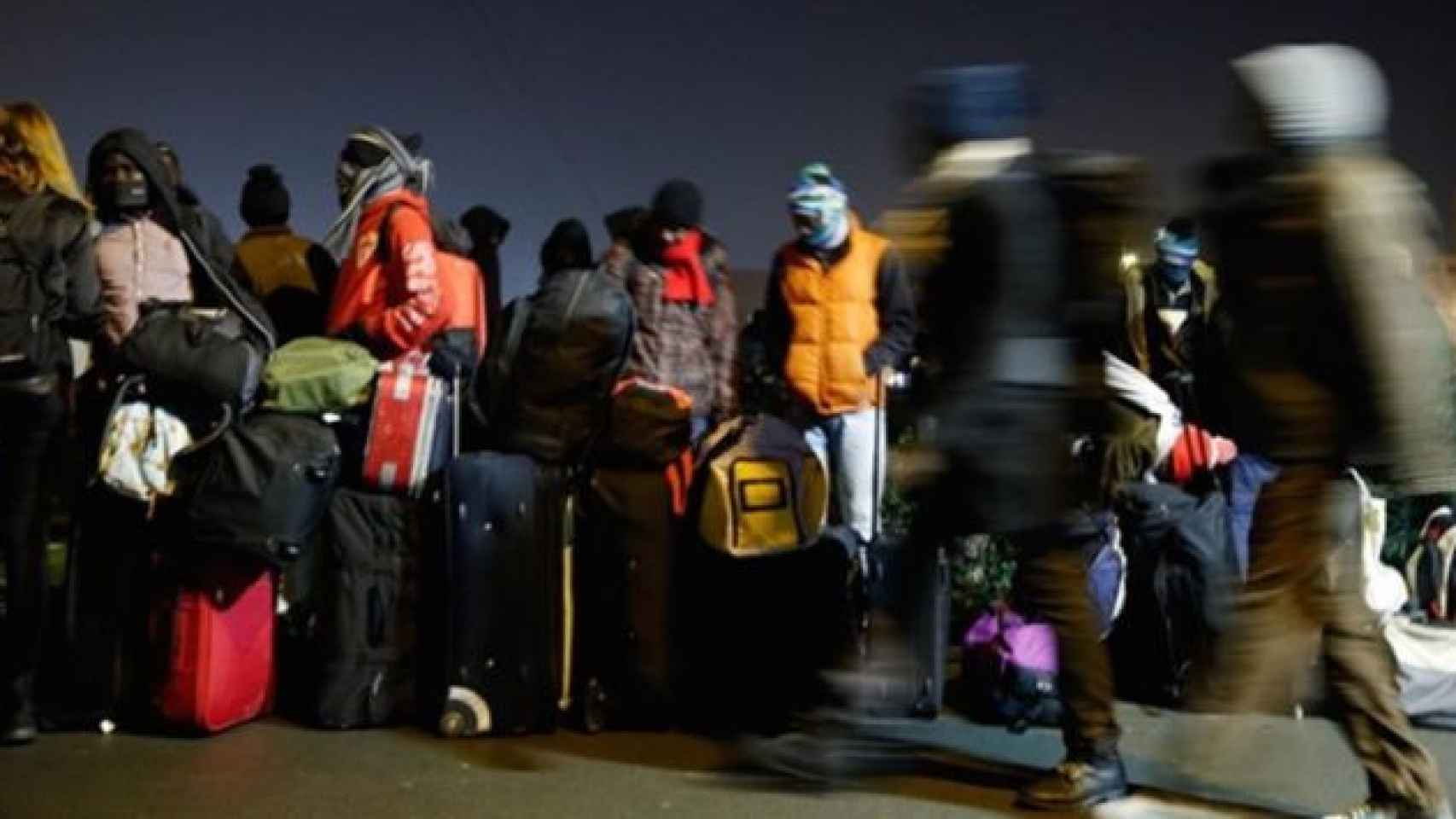 Decenas de personas hacen cola con sus maletas y mochilas en el campamento de refugiados de Calais (Francia) al inicio del desalojo / EFE