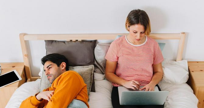 Una chica navega por internet mientras su pareja descansa en la cama / FREEPIK