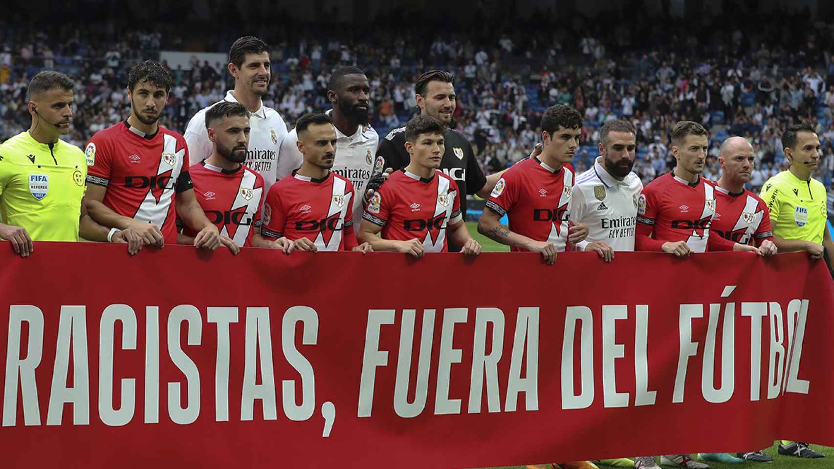 Real Madrid y Rayo Vallecano, acompañados de los árbitros, sostienen una pancarta en apoyo a Vinicius / EFE