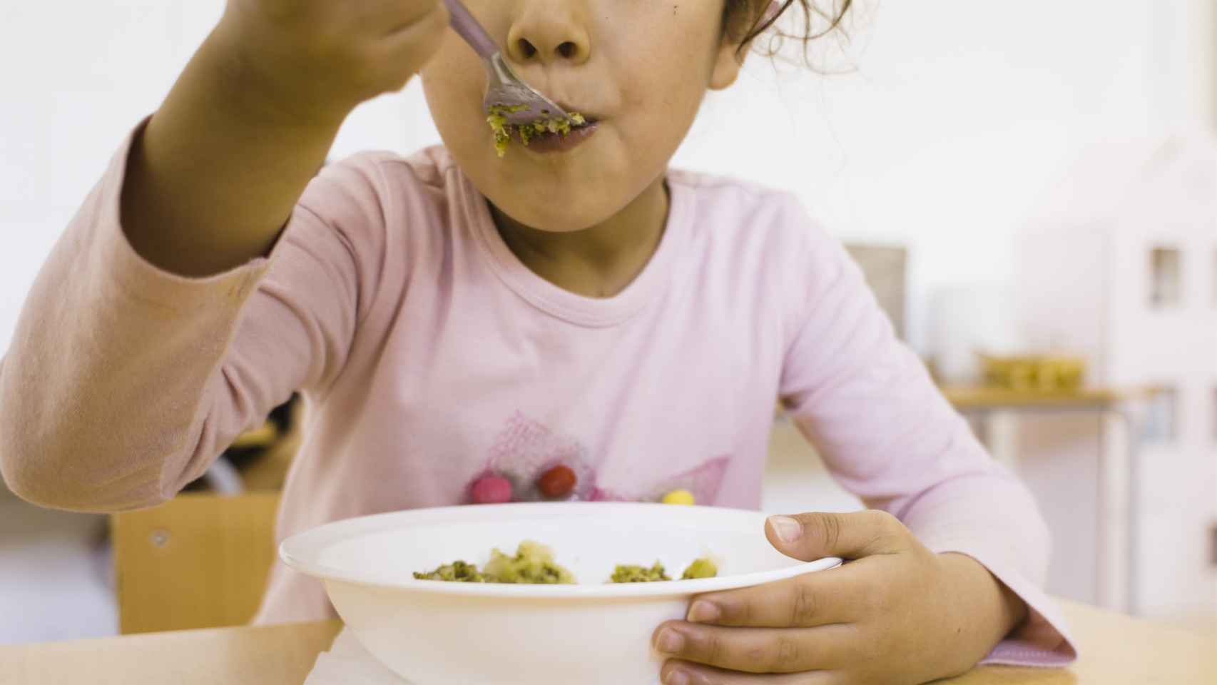 Una niña comiendo en un comedor escolar