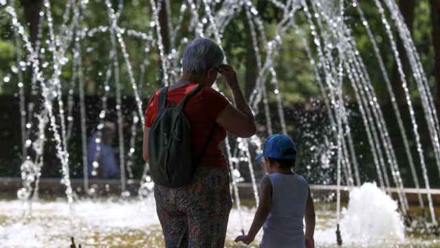 Niños y adultos se refrescan a la sombra, junto a las fuentes públicas del parque del Retiro en una jornada marcada por las altas temperaturas