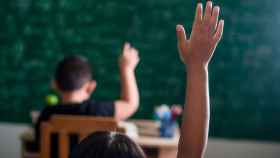 Dos alumnos levantan la mano en un aula
