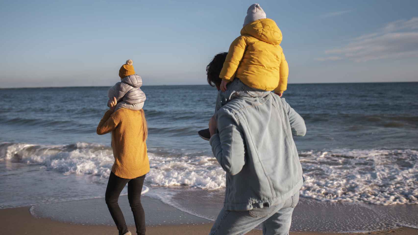 Dos personas con niños en brazo pasean por la playa