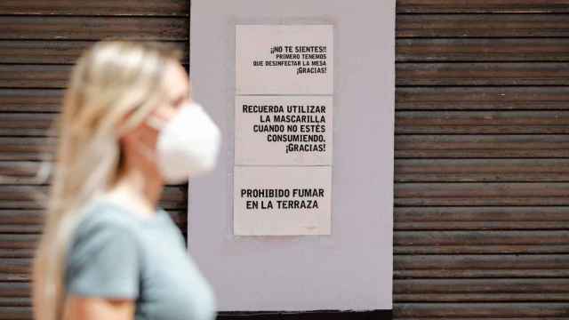 Una mujer pasa por enfrente de la fachada de un bar con carteles que recuerdan algunas de las medidas adoptadas por la hostelera como consecuencia de la pandemia. / EFE