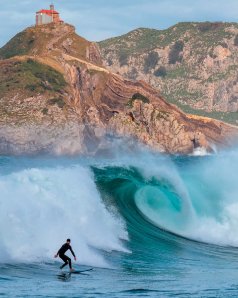 Un hombre practica surf en Bakio con Gaztelugatxe al fondo / Gobierno vasco