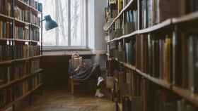 Una mujer sentada lee un libro en una biblioteca / PEXELS
