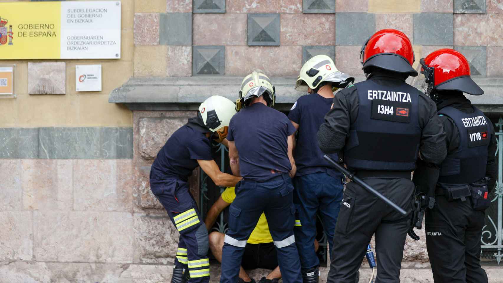 Efectivos de bomberos, liberan a uno de los dos jóvenes que esta mañana se habían atado por el cuello a la reja de la fachada de la Subdelegación del Gobierno en Bilbao, durante una concentración convocada por Ernai.