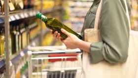 Una mujer con un bote de aceite de oliva en un supermercado.