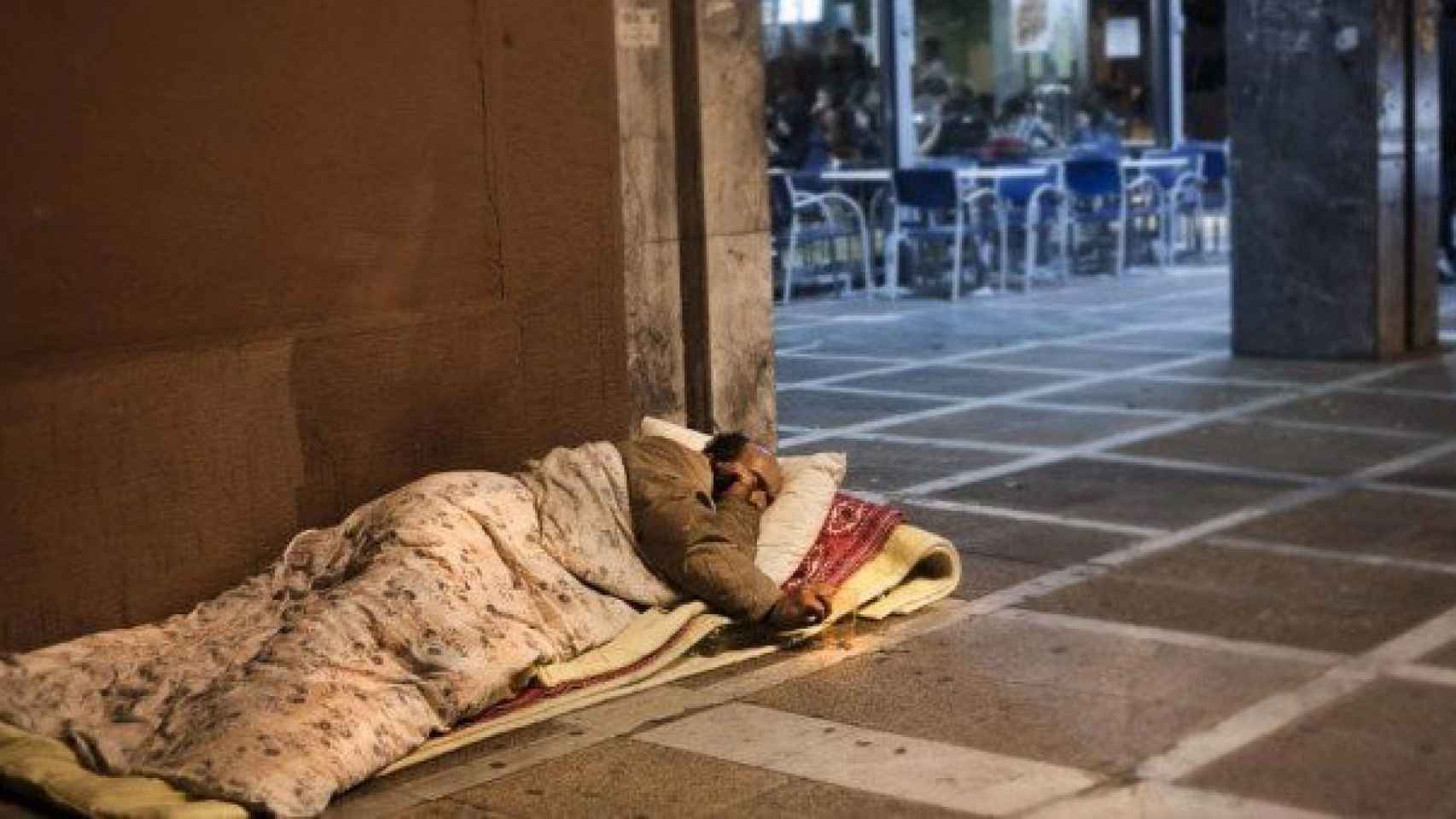 Un hombre sin techo duerme en la acera, junto a una cafetería / EFE