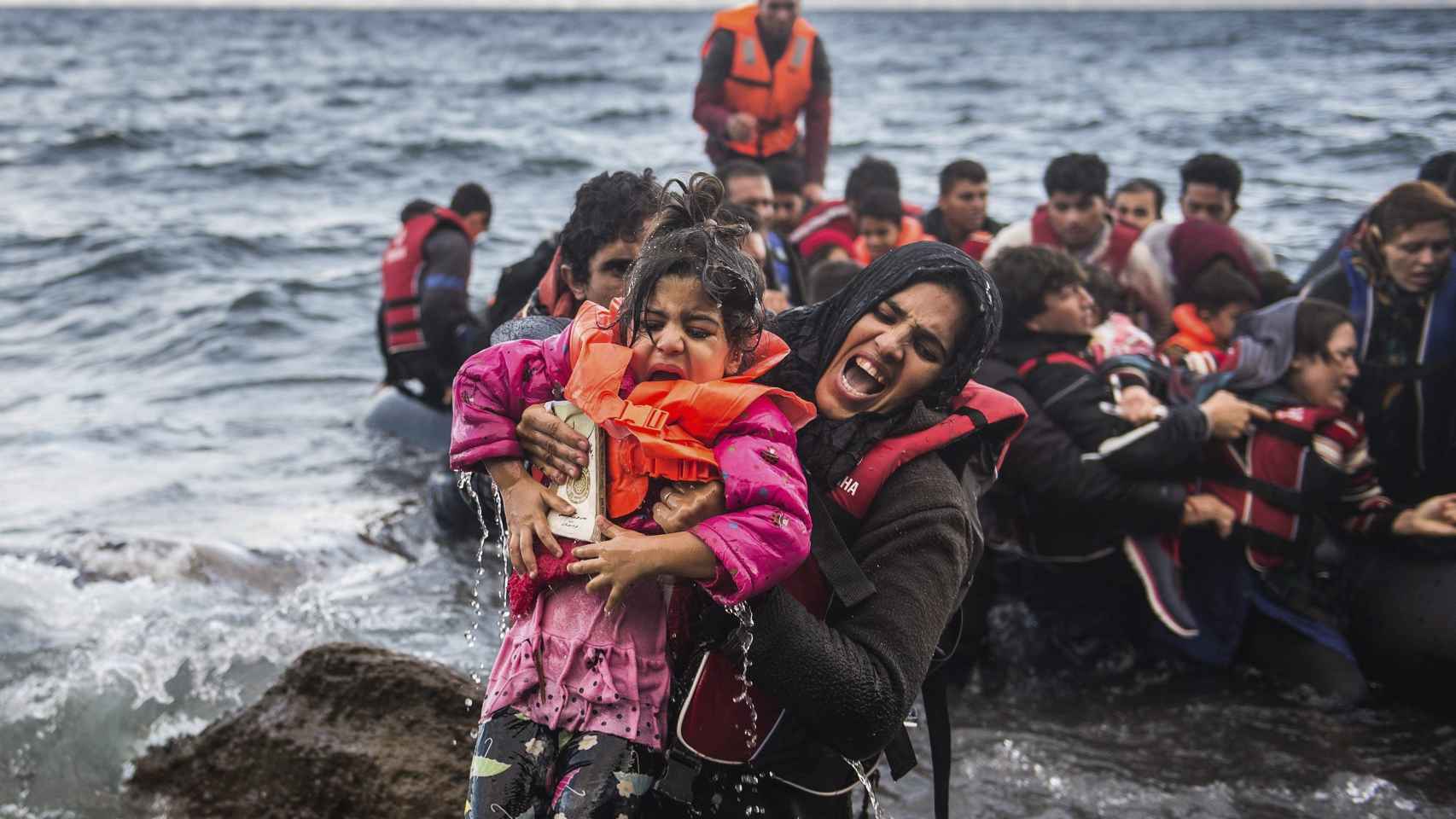 Una refugiada salta de una lancha neumática con su hija en brazos tras alcanzar la costa, en la isla de Lesbos. Octubre de 2015 / EFE/Filip Singer