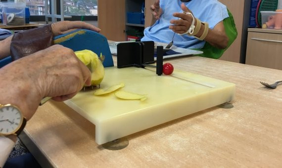 Roser corta una manzana en primer plano y otro paciente usa una cuchara al fondo / PABLO ALEGRE