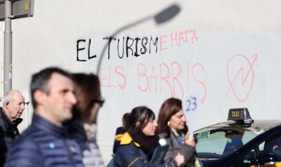 Un grupo de turistas pasa junto a la pintada xenófoba del Eixample / ÁLVARO VENTURA