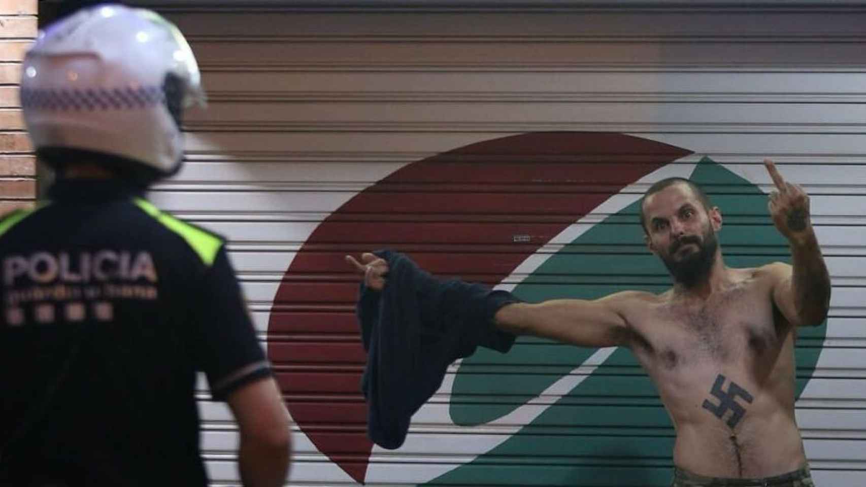 Un joven ultra, con un esvástica en el pecho, hace la peineta ante un agente de policía.