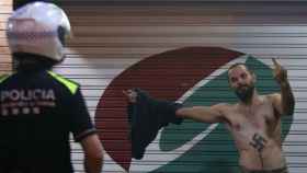 Un joven ultra, con un esvástica en el pecho, hace la peineta ante un agente de policía.