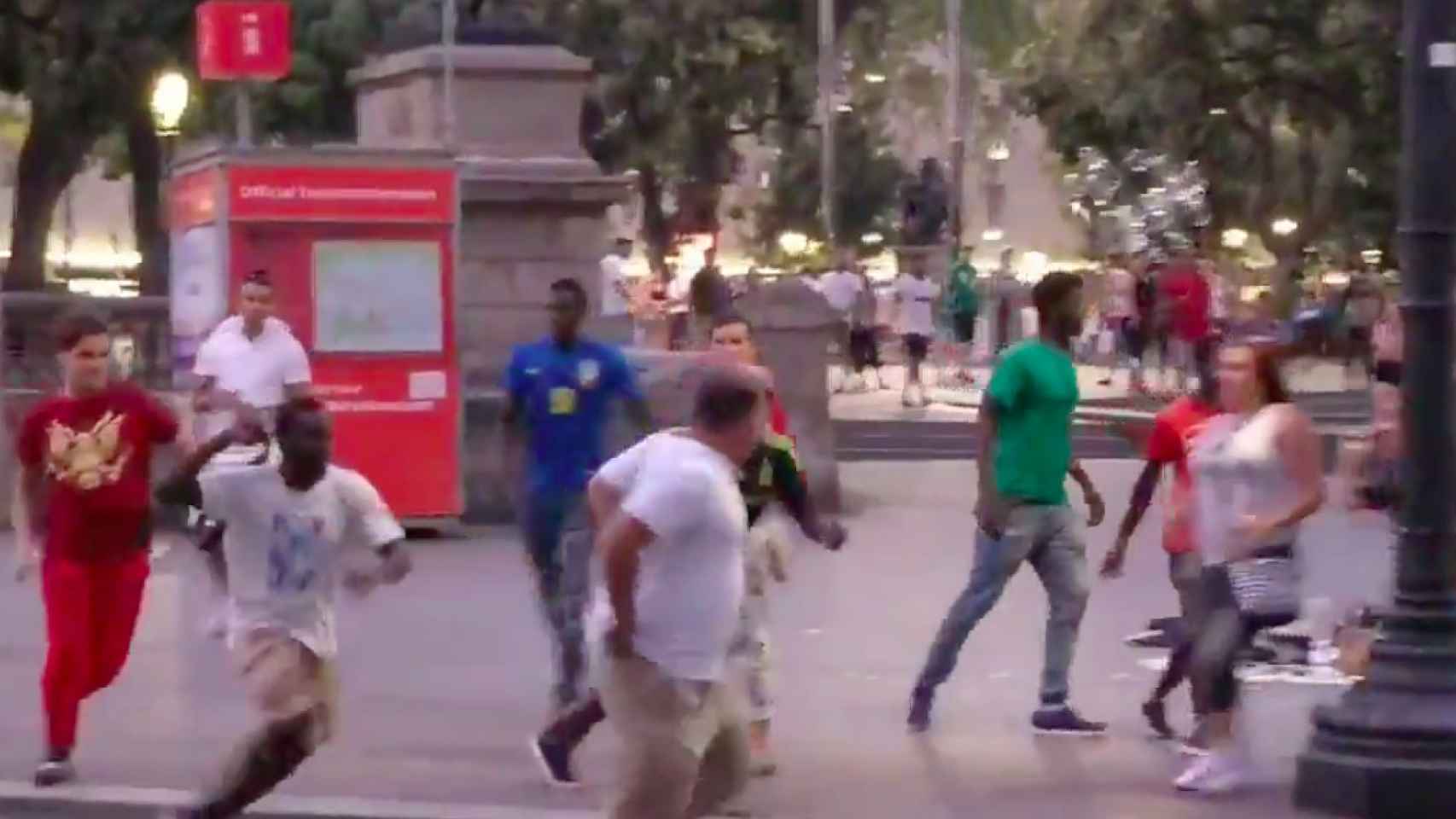 Un mantero, con camiseta blanca y un cinturón, persigue al turista en la plaza de Catalunya / TWITTER @AKur0mu