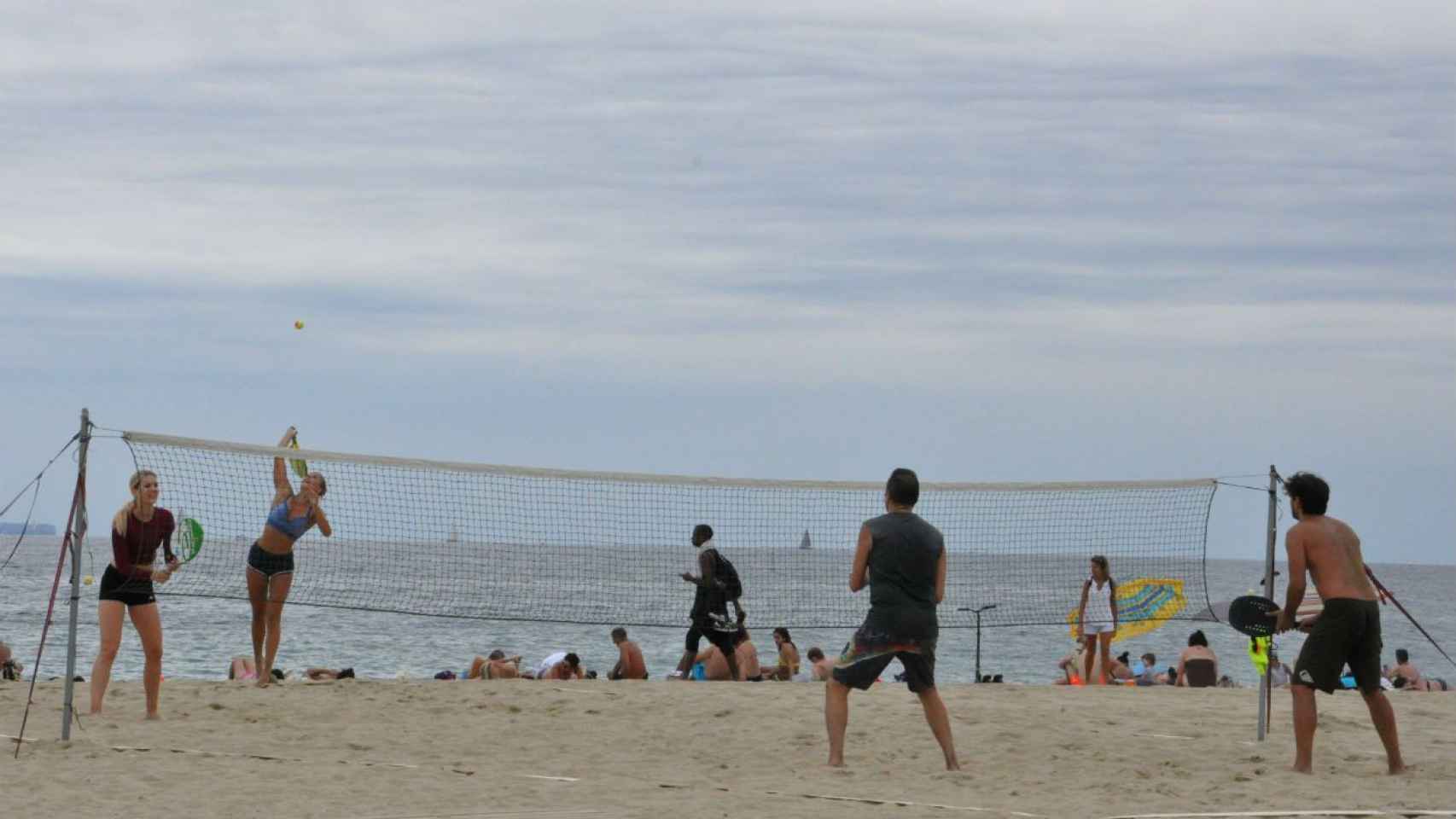 Dos parejas, una de chicas y otra de chicos, practicando tenis playa en el Beach Tennis Barcelona / MIKI
